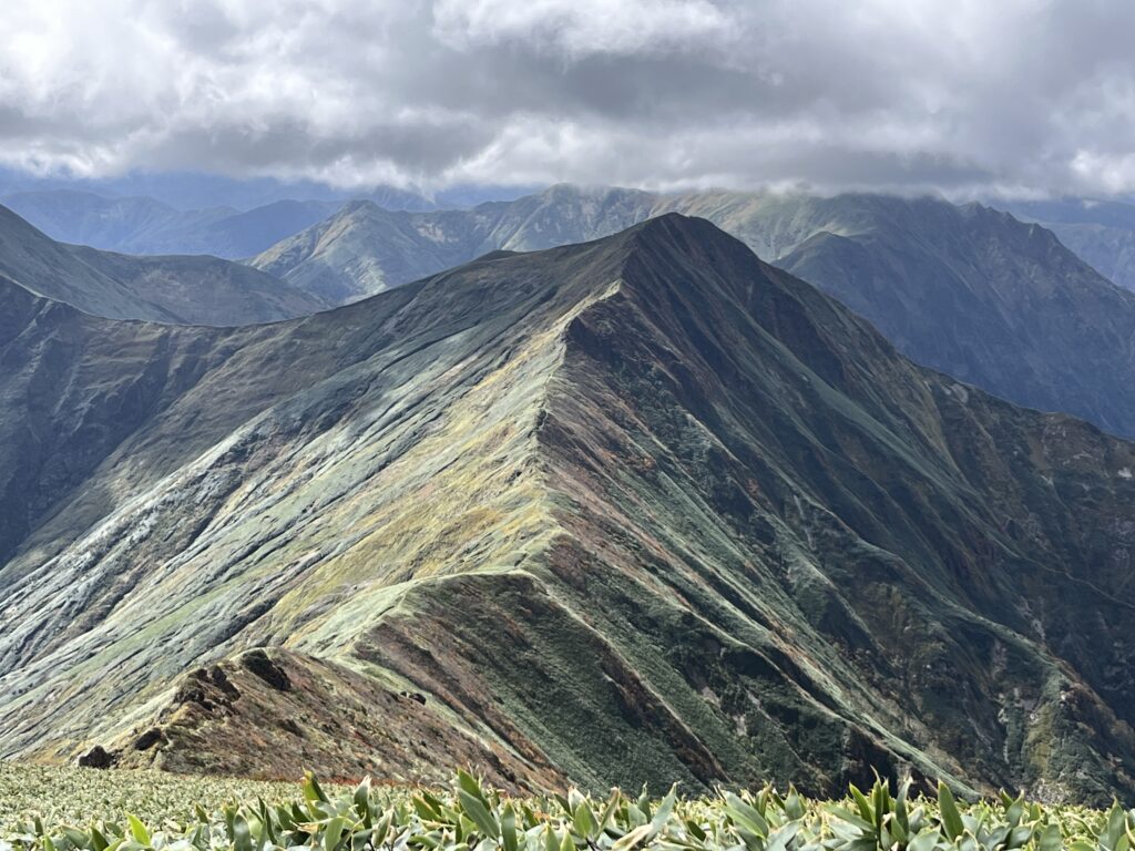 谷川岳の山頂付近から見た、光の当たる稜線と重なる山々
